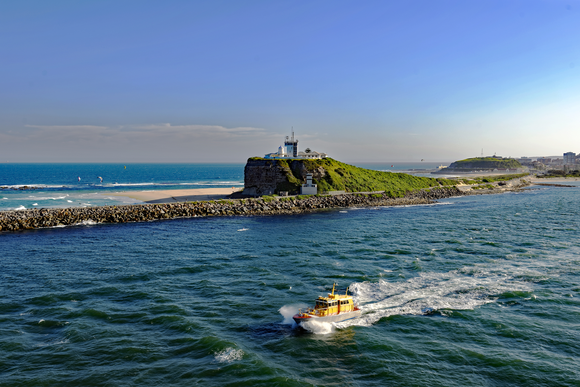 A pilot cutter vessel leaves Newcastle on the water past Nobbys Lighthouse