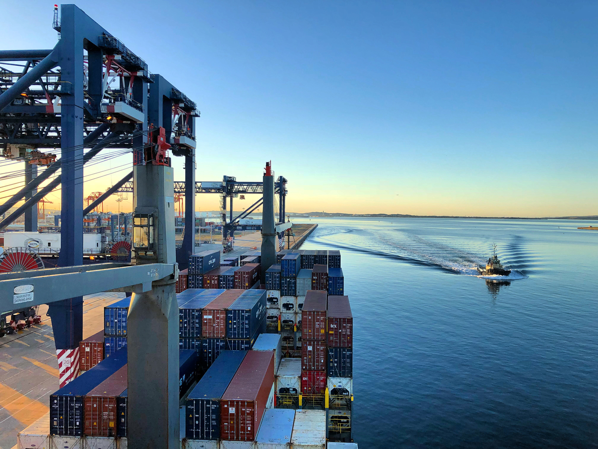 A small cutter vessel on the water passing a large docked container ship