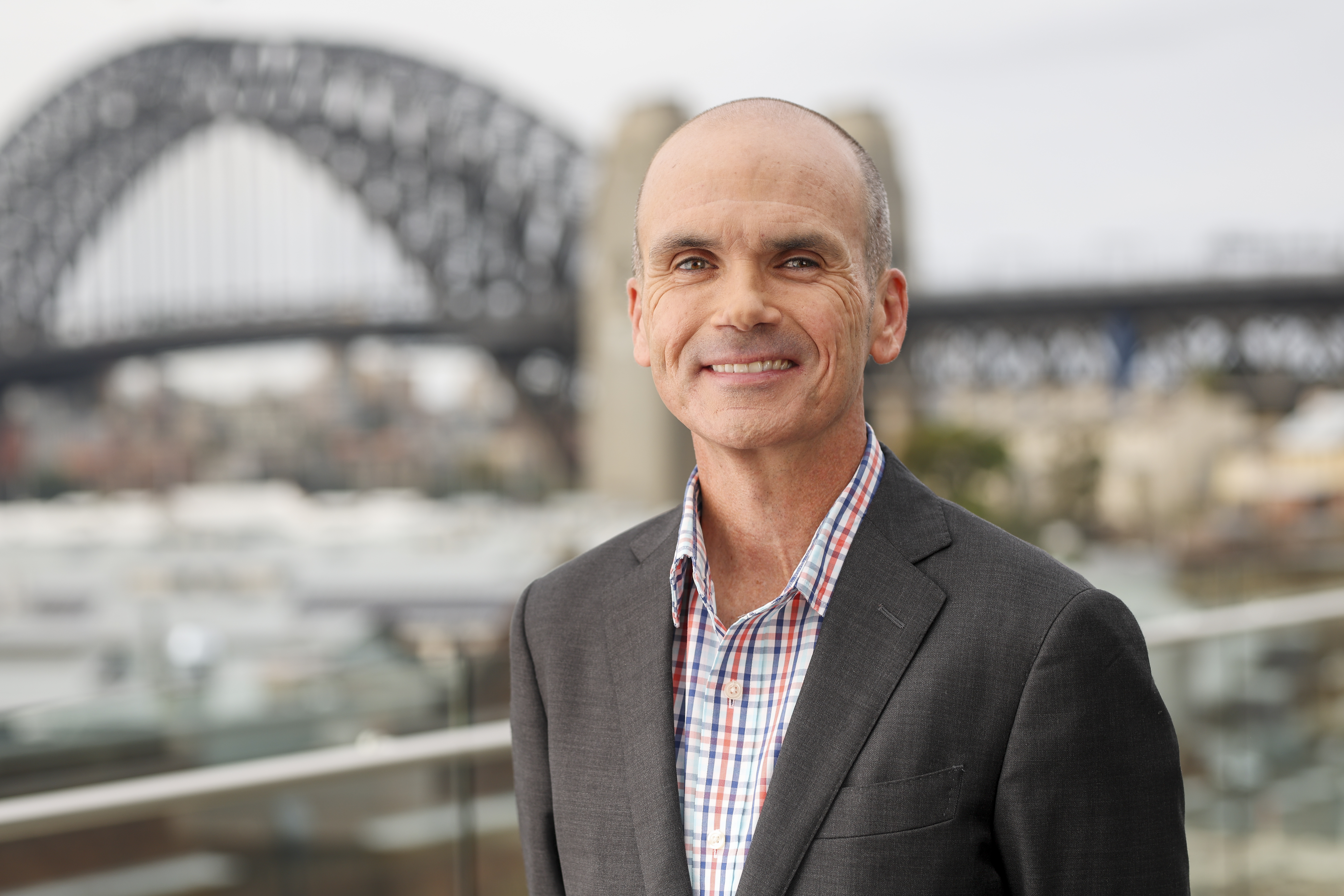 Headshot of a man in business attire standing with the Sydney Harbour Bridge in the background