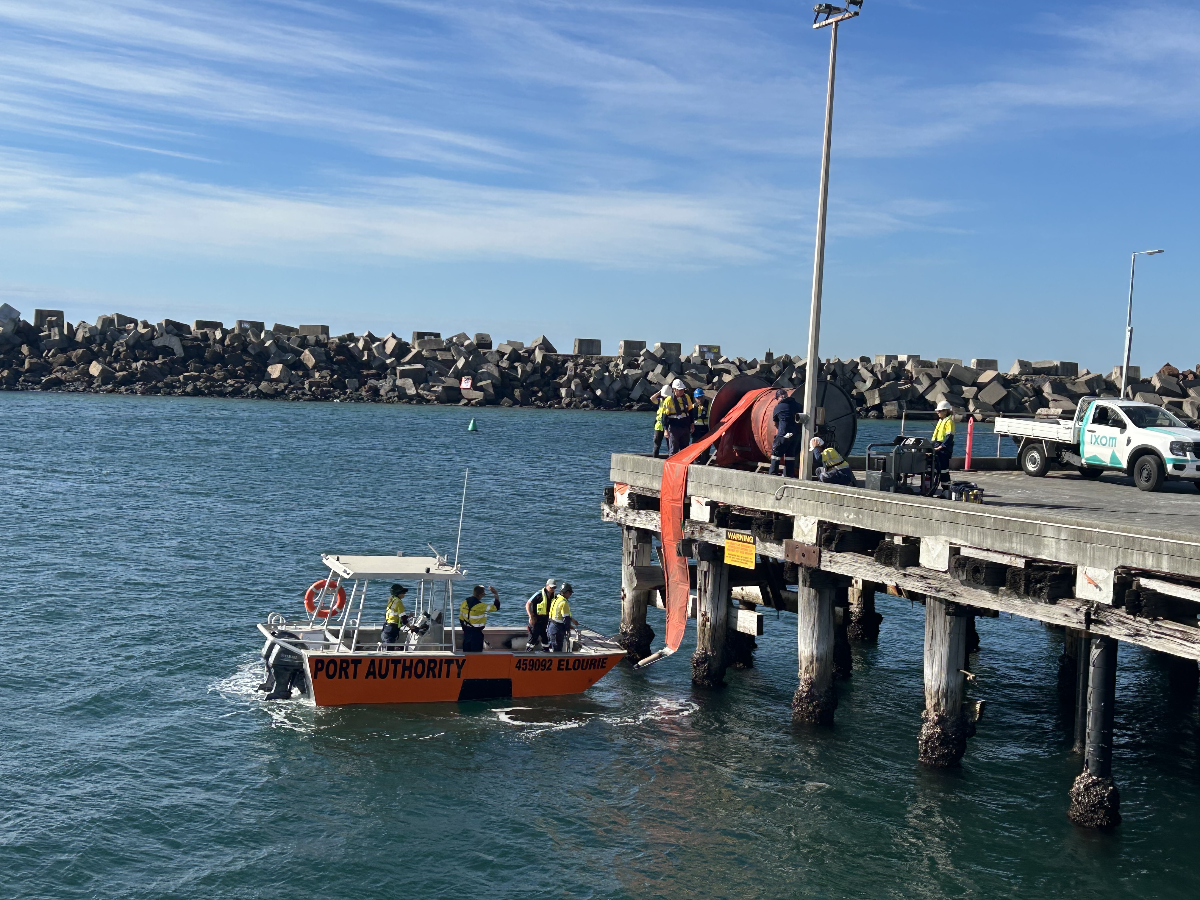 A Port Authority vessel on the water at Port Kembla, with staff deploying a boom