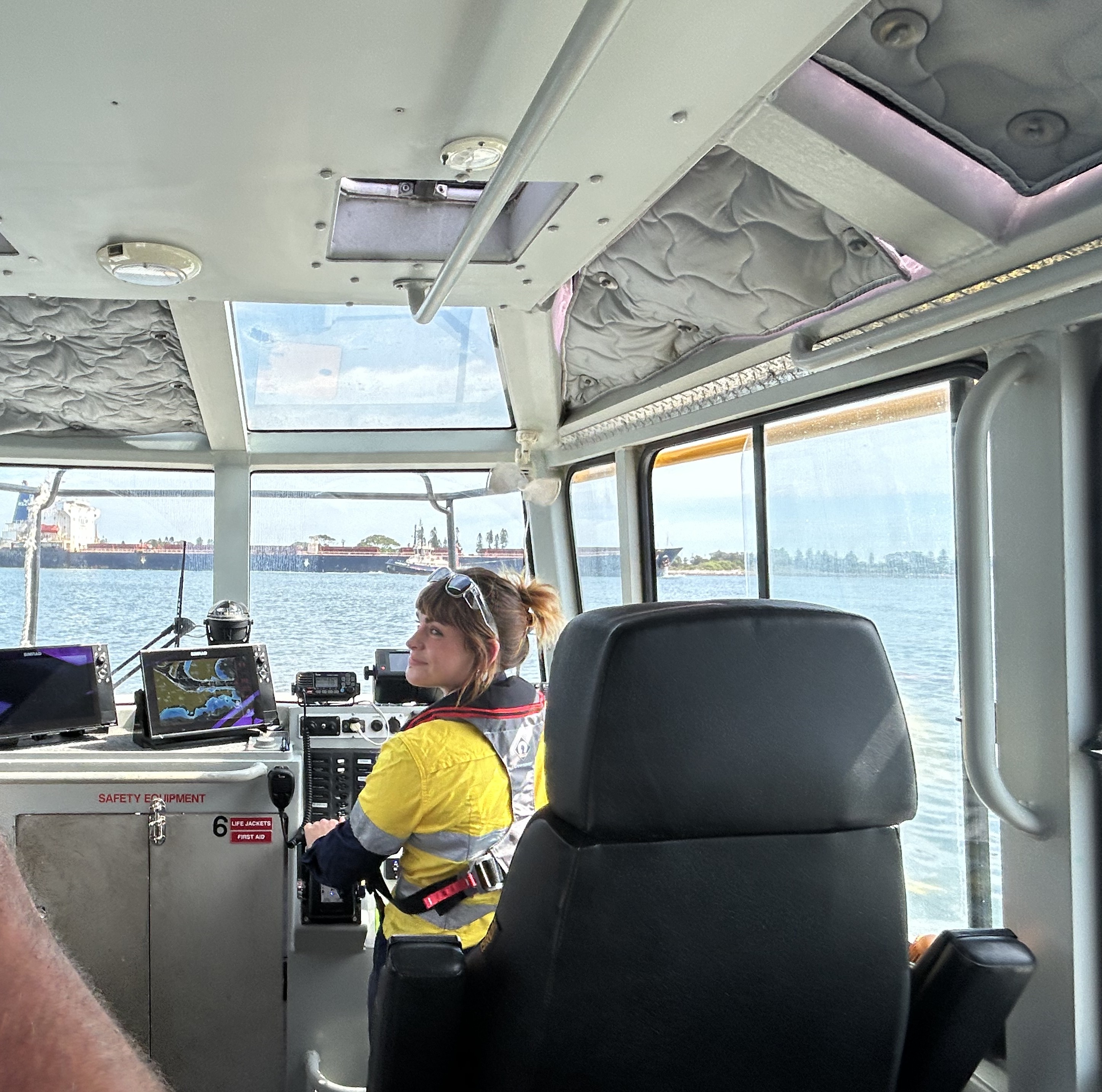 A female Port Officer stands at the controls of a cutter vessel overlooking Newcastle Harbour