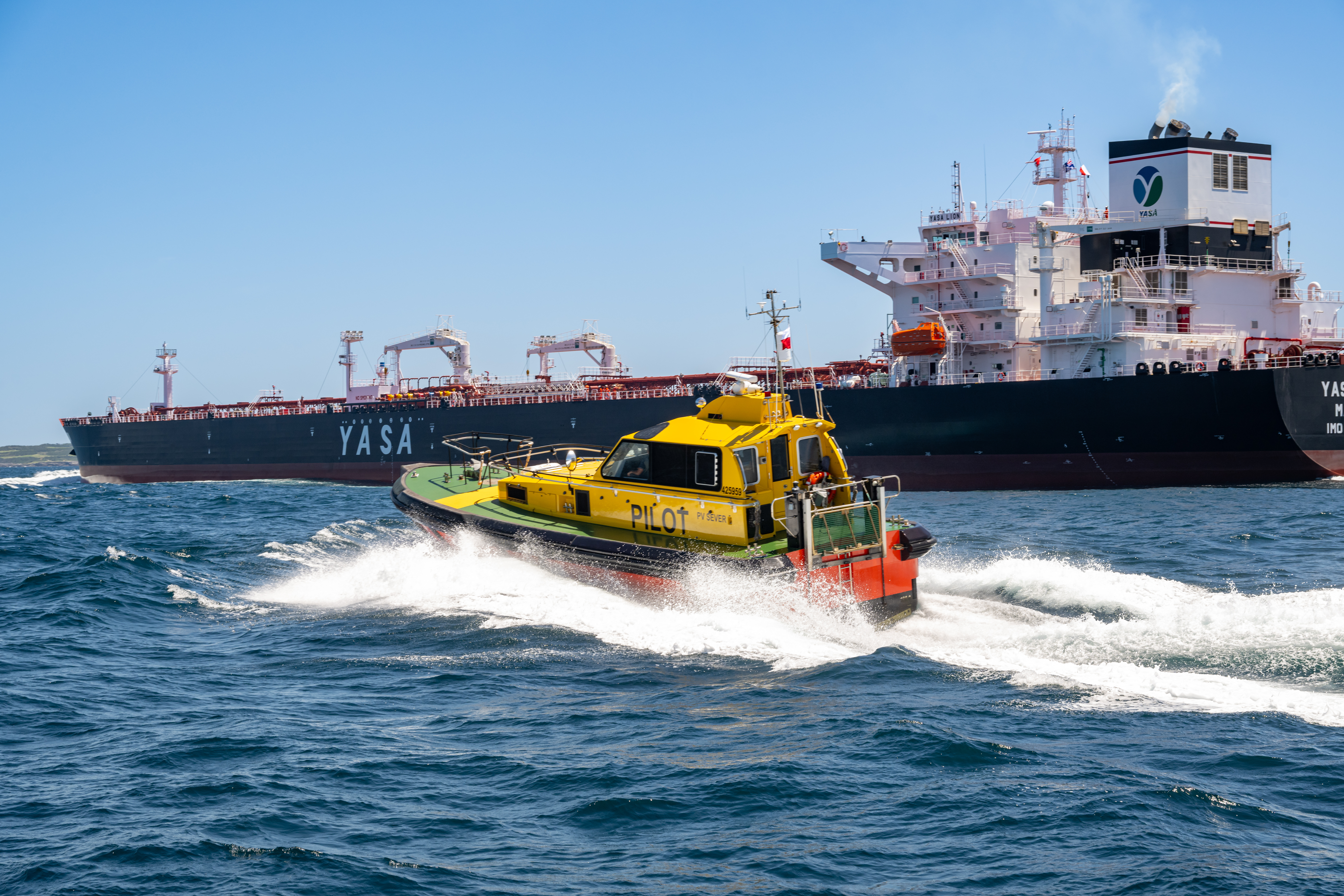 A yellow pilot vessel approaches a large cargo vessel 