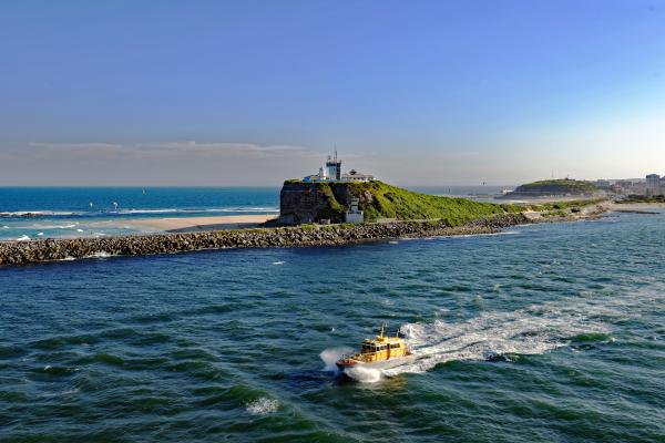A pilot cutter vessel leaves Newcastle on the water past Nobbys Lighthouse