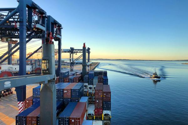 A small cutter vessel on the water passing a large docked container ship