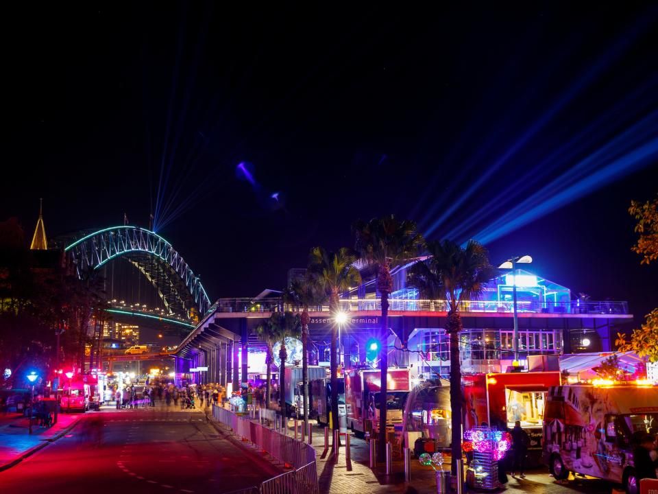 Pink and blue lights shine from the Overseas Passenger Terminal with the Harbour Bridge in the distance during Vivid Sydney