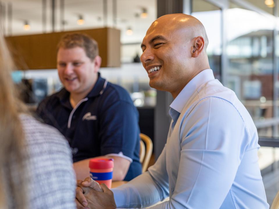 A man in a business shirt sitting at a table smiling at colleagues