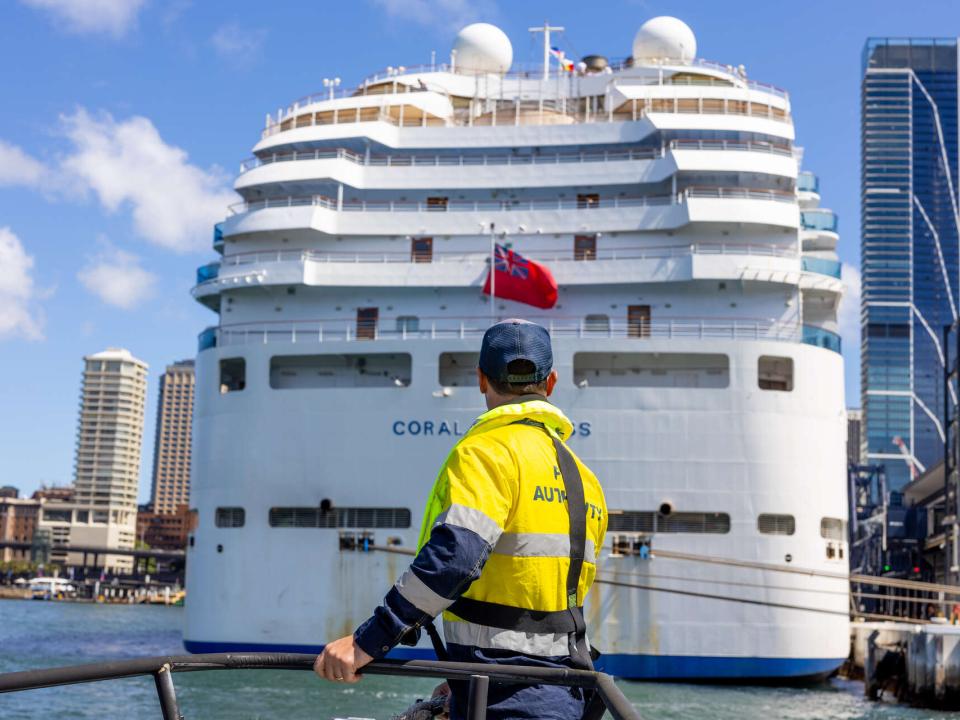 A Port Authority employee on board a vessel looks up at a large cruise ship docked at the Overseas Passenger Terminal