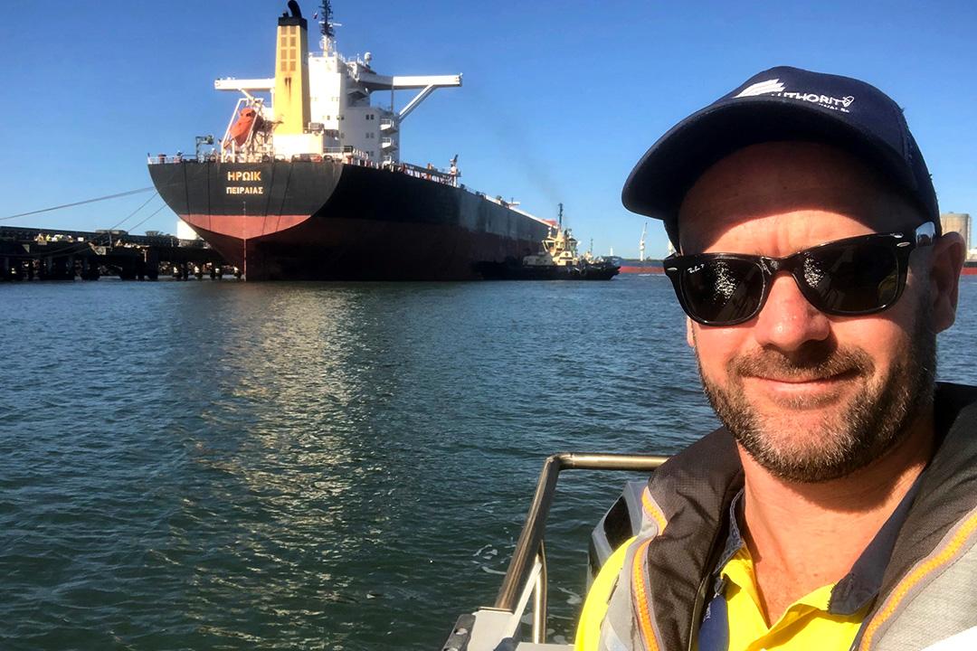 Jimmy McGrath smiles at camera with a bulk carrier on the water behind him