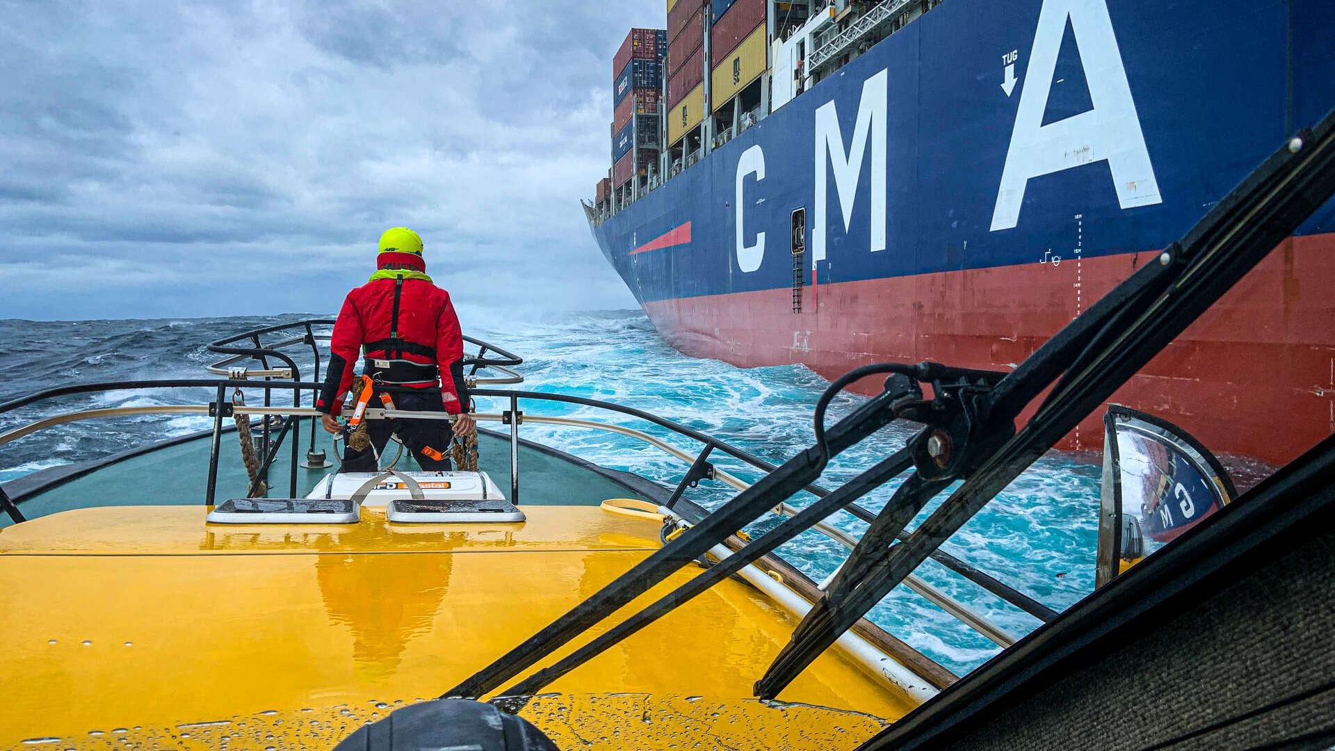 A pilot stands at the front of a cutter vessel getting ready to embark a container ship on the wa