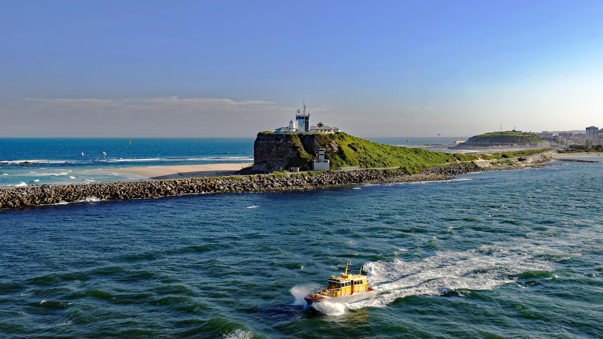 A pilot cutter vessel leaves Newcastle on the water past Nobbys Lighthouse