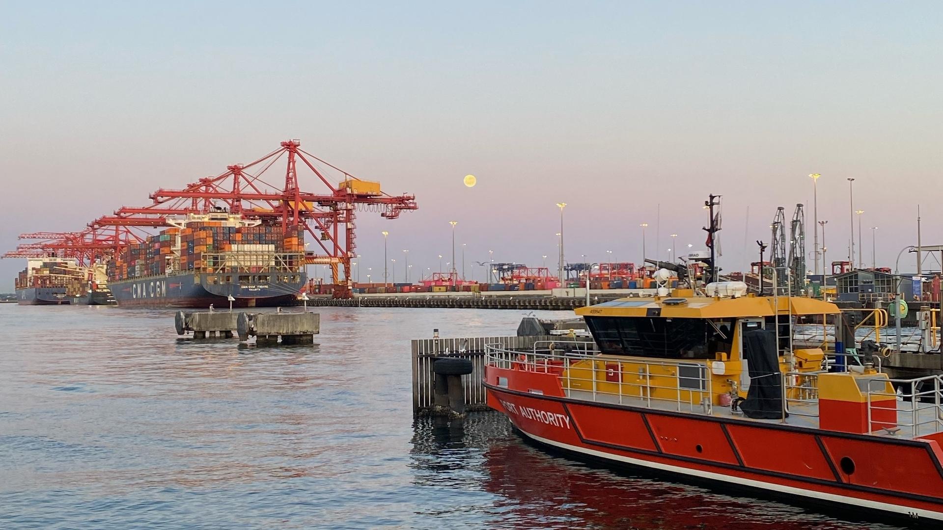 Port Authority vessel on the water at Port Botany with cranes in the distance and the moon in the sky at sunset