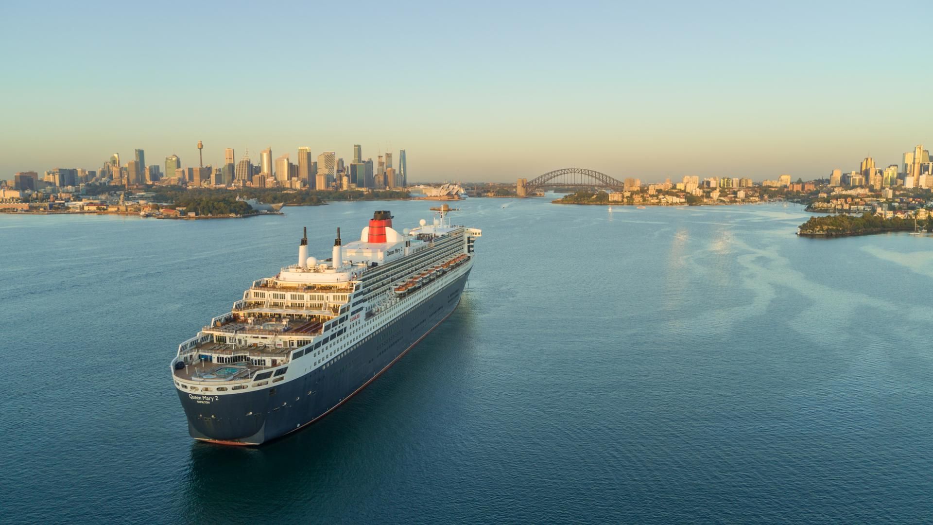 Aerial of Queen Mary 2 entering Sydney Harbour at sunrise with CBD and Harbour Bridge in distance