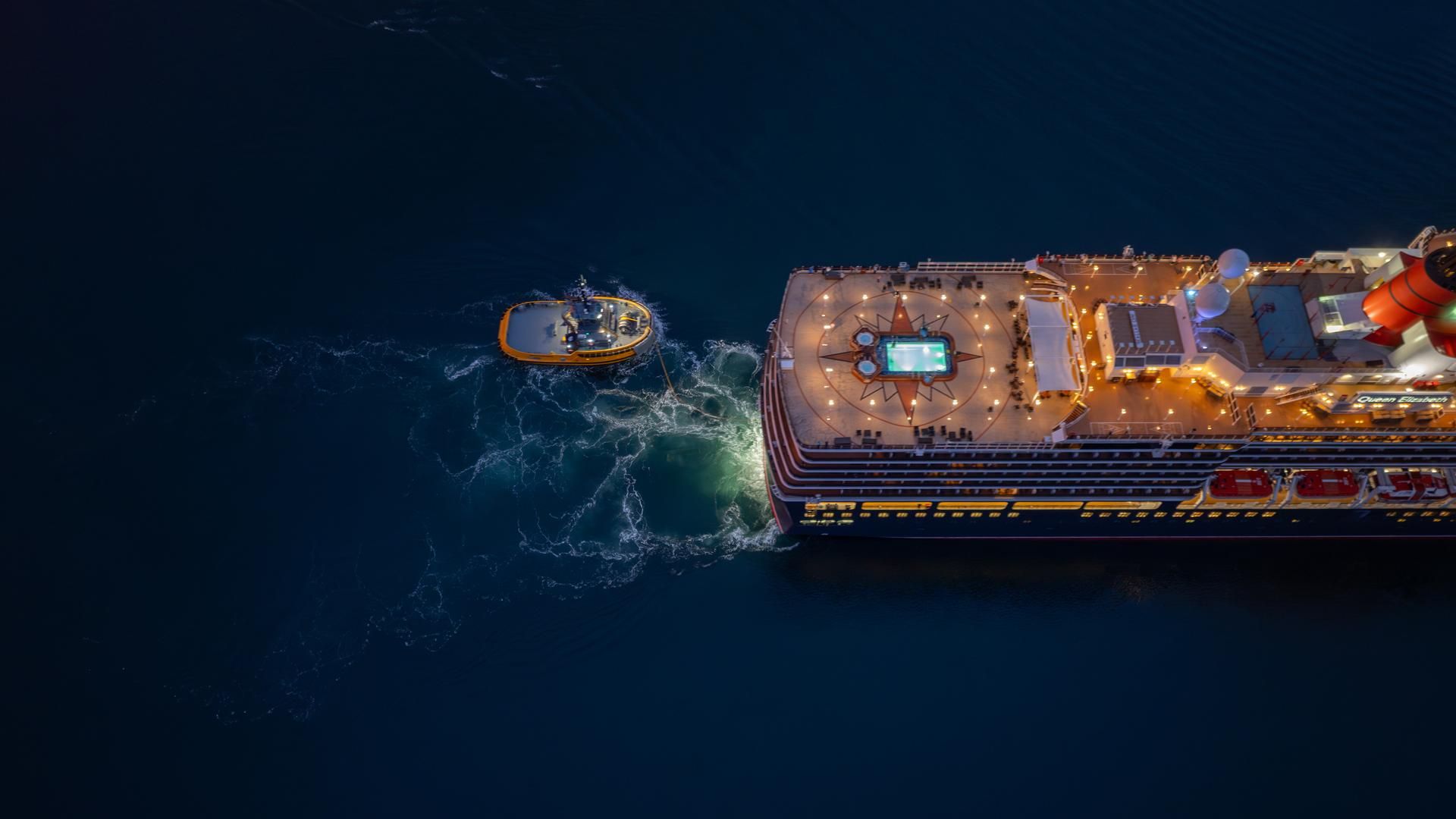 Birds eye view looking down on a cruise ship with a tug behind