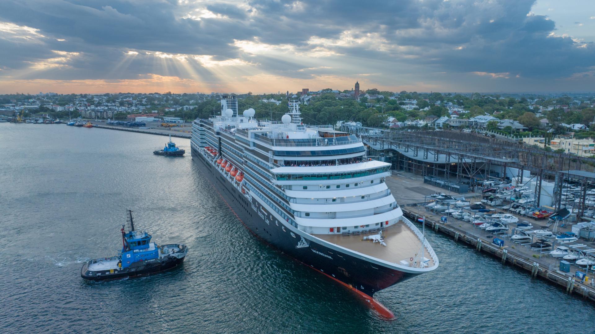 A cruise ship comes alongside White Bay Cruise Terminal, guided into position by two tugs, and surrounding residential area in the distance