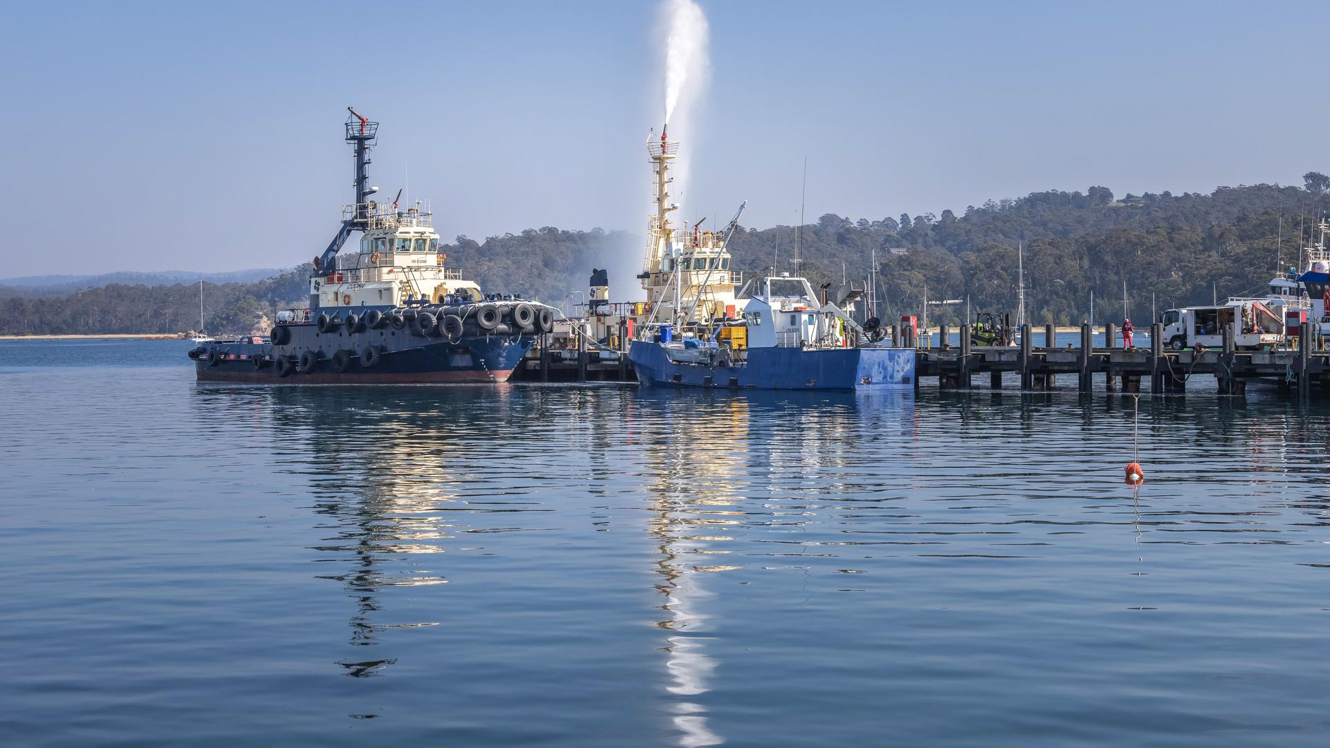 A tug and other vessels on the water on a clear day, with one vessel spraying water in the air