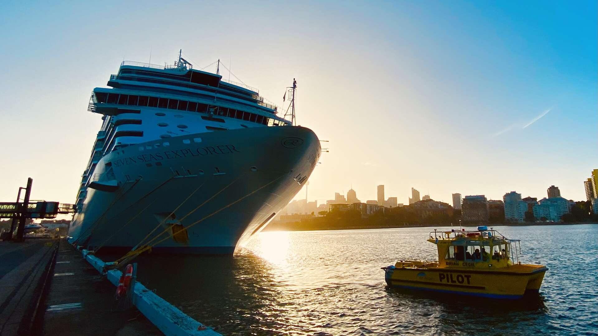 A cruise ship berthed at White Bay at sunrise with a Port Authority vessel in front