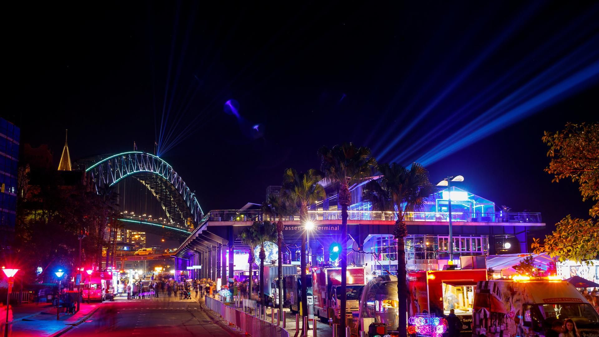 Pink and blue lights shine from the Overseas Passenger Terminal with the Harbour Bridge in the distance during Vivid Sydney