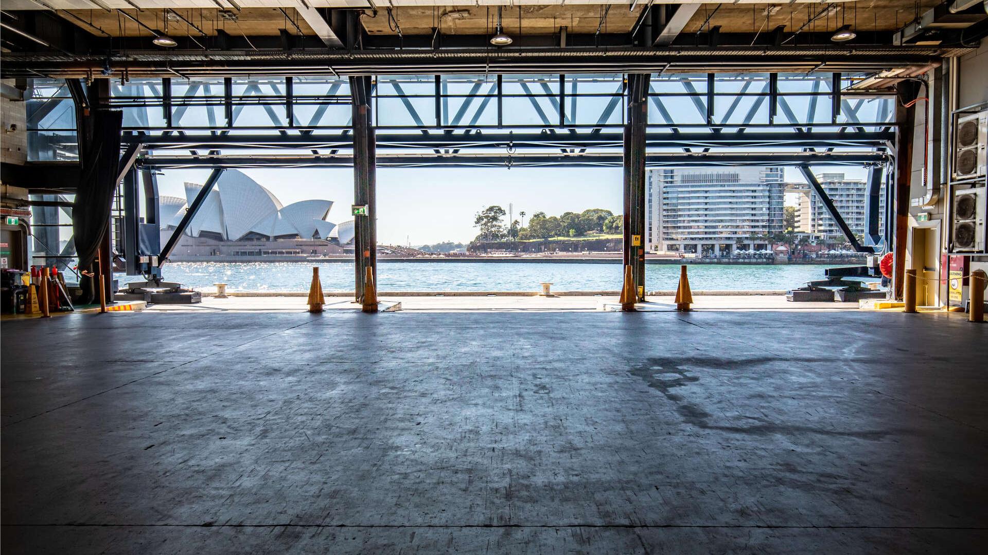 The industrial interior of the Cargo Hall looking onto Sydney Harbour and the Opera House on the left