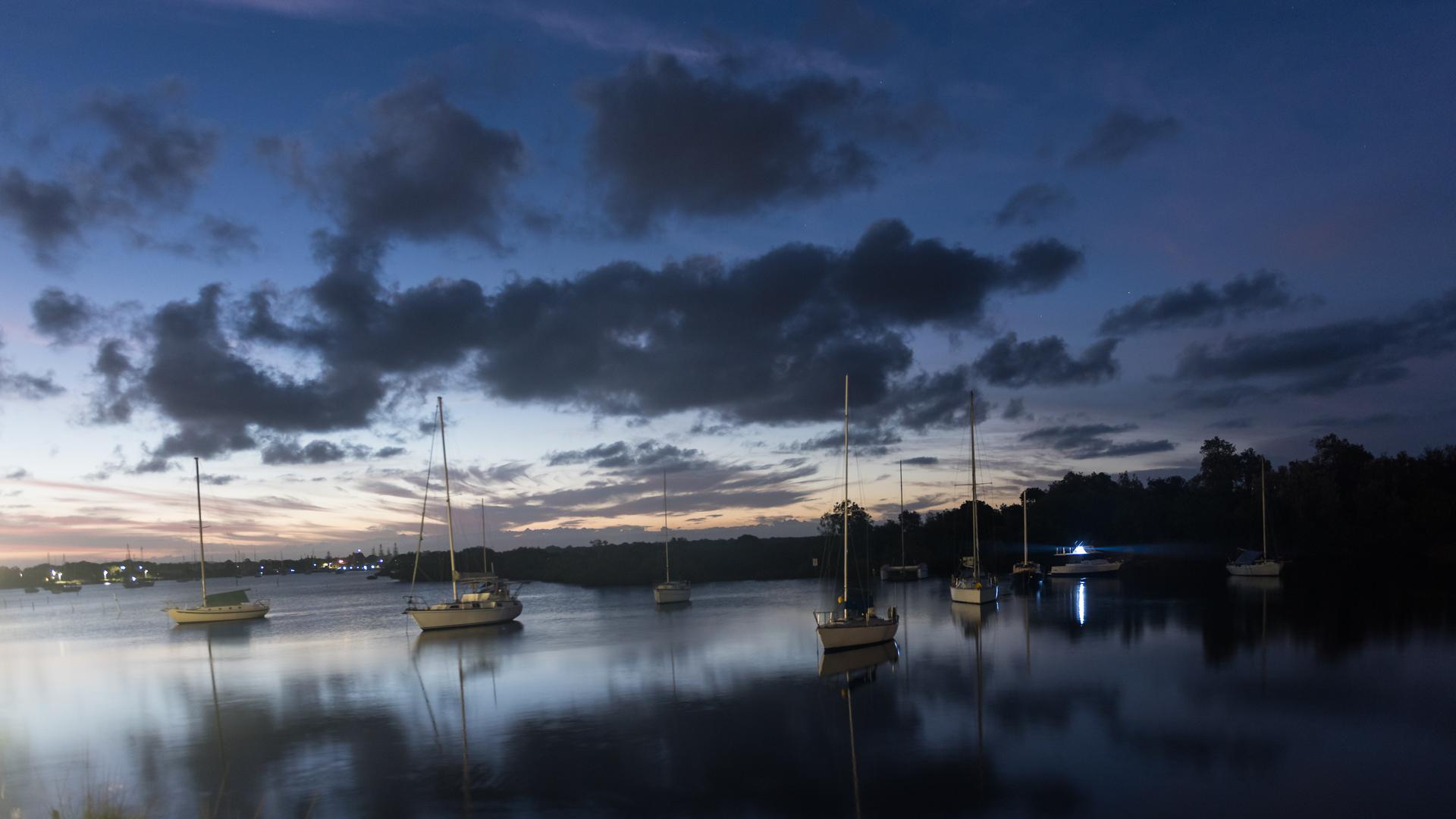 Sailing boats on the water at dusk with moody clouds in the sky