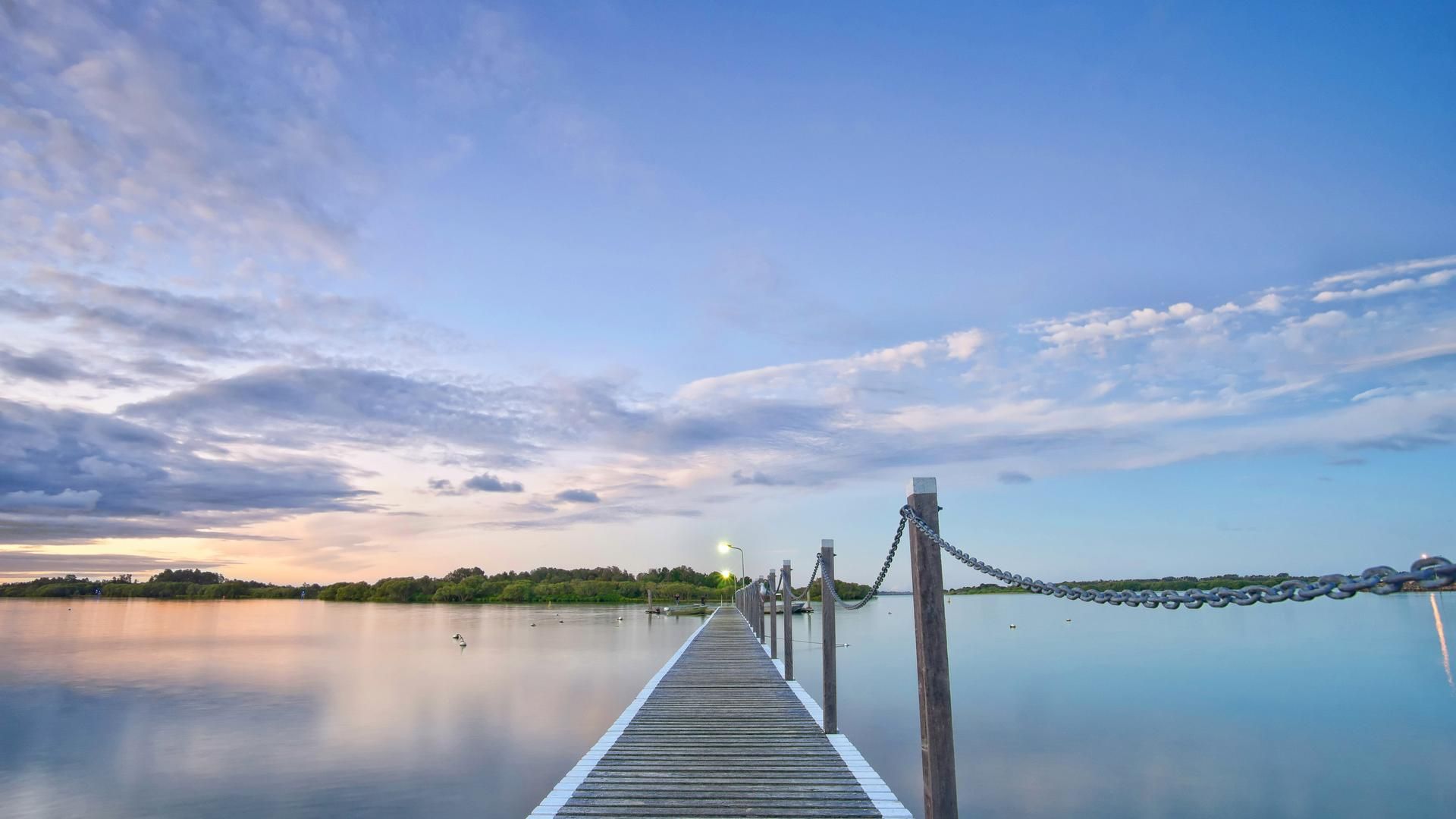 Looking along a pier to water with beautiful soft blue and pink sky and reflections on the still water