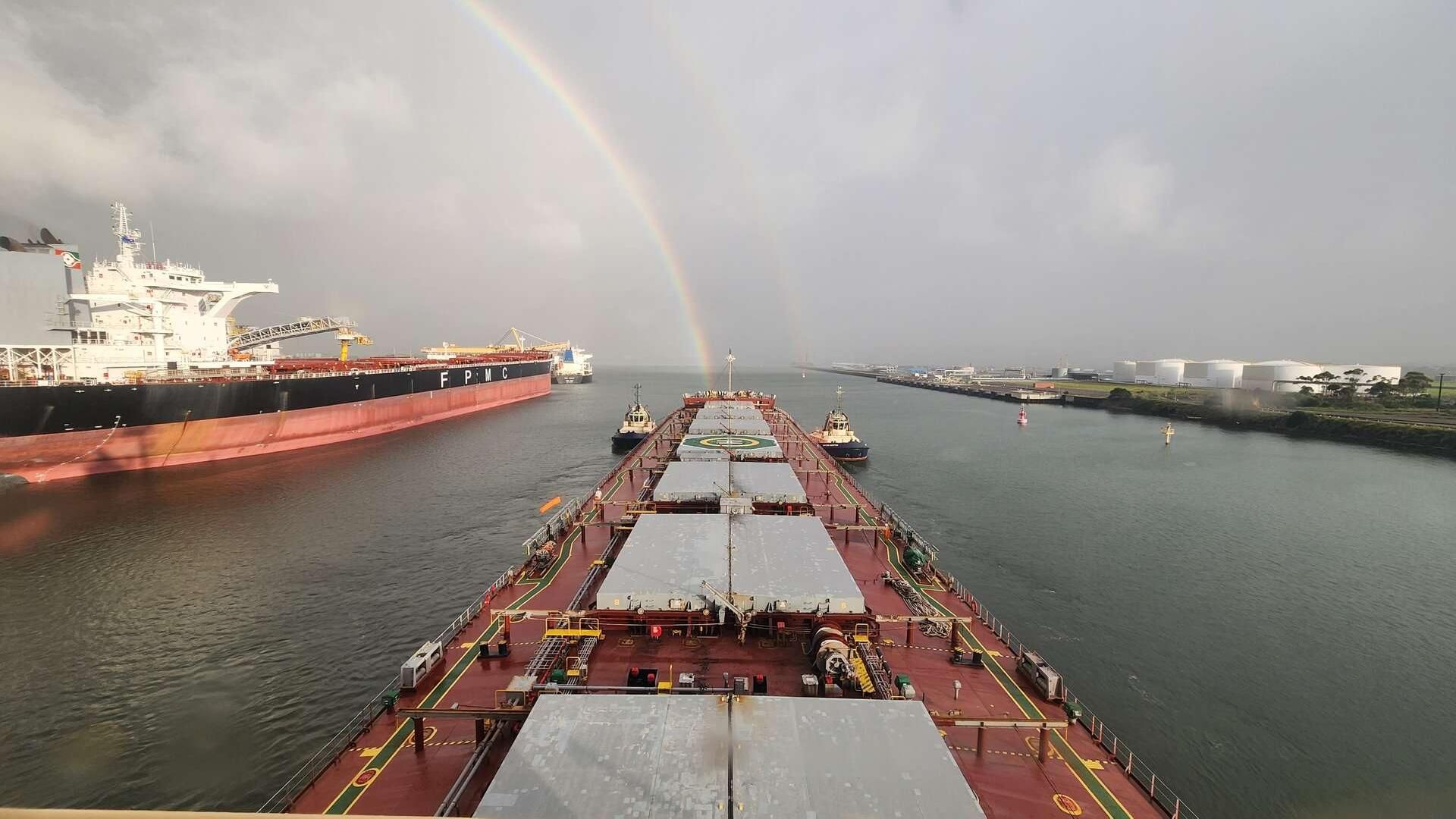 View from the bridge of a cargo ship in Newcastle Harbour with a rainbow in the distance appearing to reach the vessel