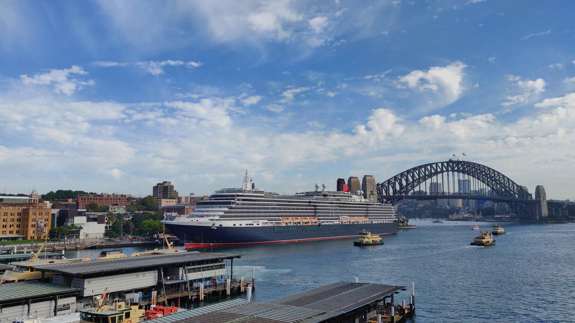 Queen Victoria cruise ship docked at Overseas Passenger Terminal on a sunny day with Circular Quay in foreground and Harbour Bridge behind the ship